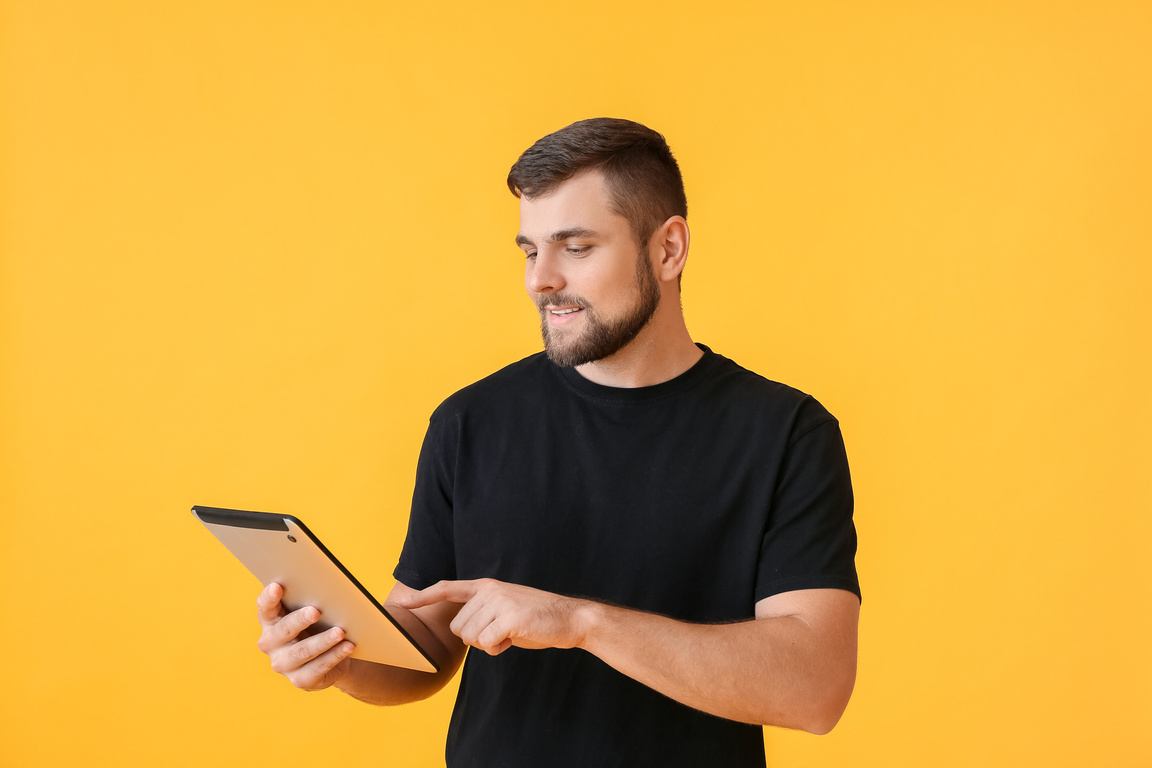 Young Man with Tablet Computer on Color Background